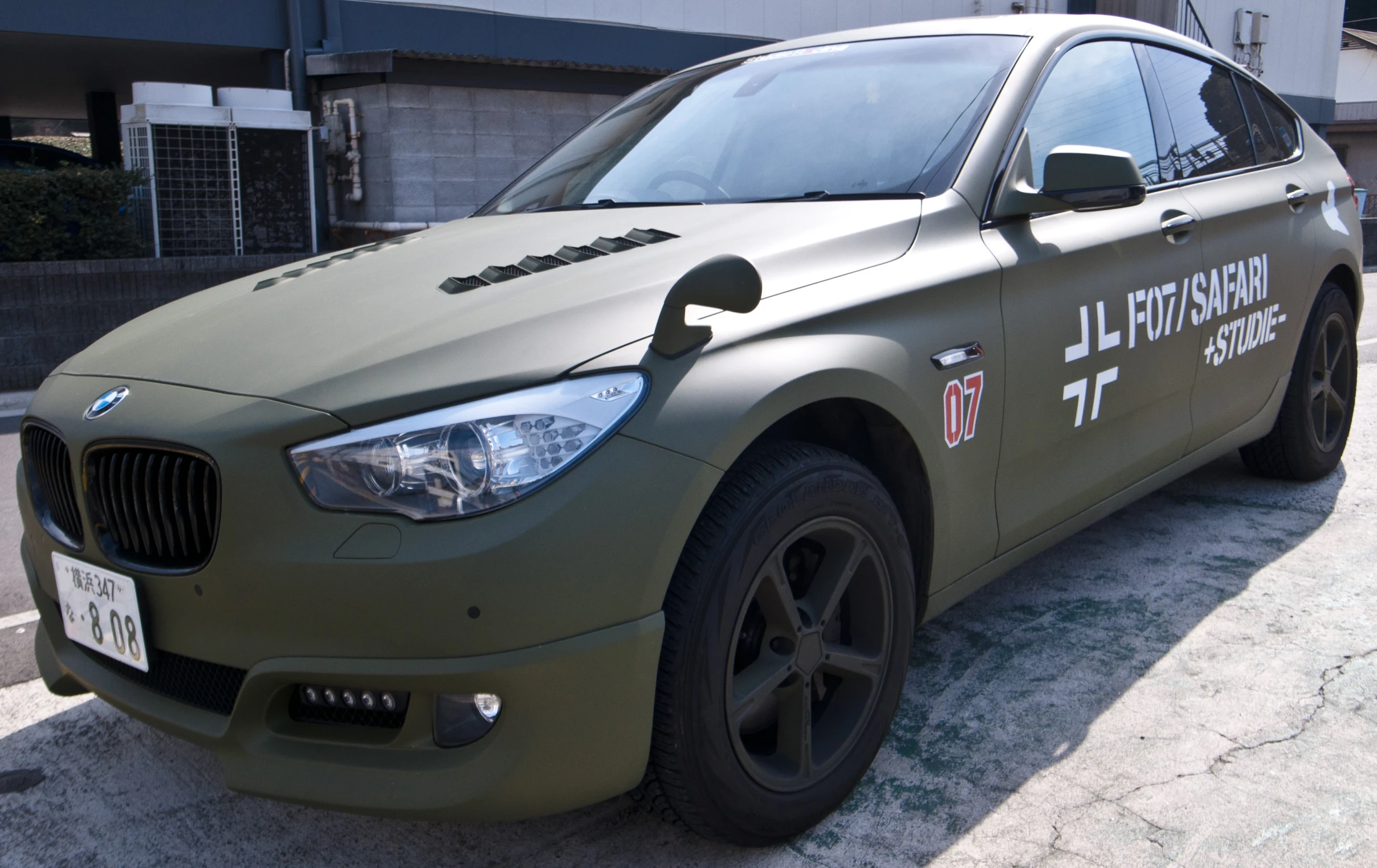 a large army green bmw is parked on the curb