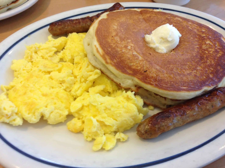 a breakfast plate topped with pancakes, sausages and scrambled eggs