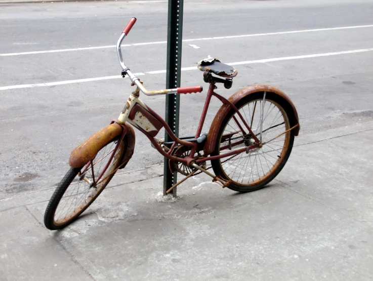 a rusty bicycle leaning on a post on a city sidewalk