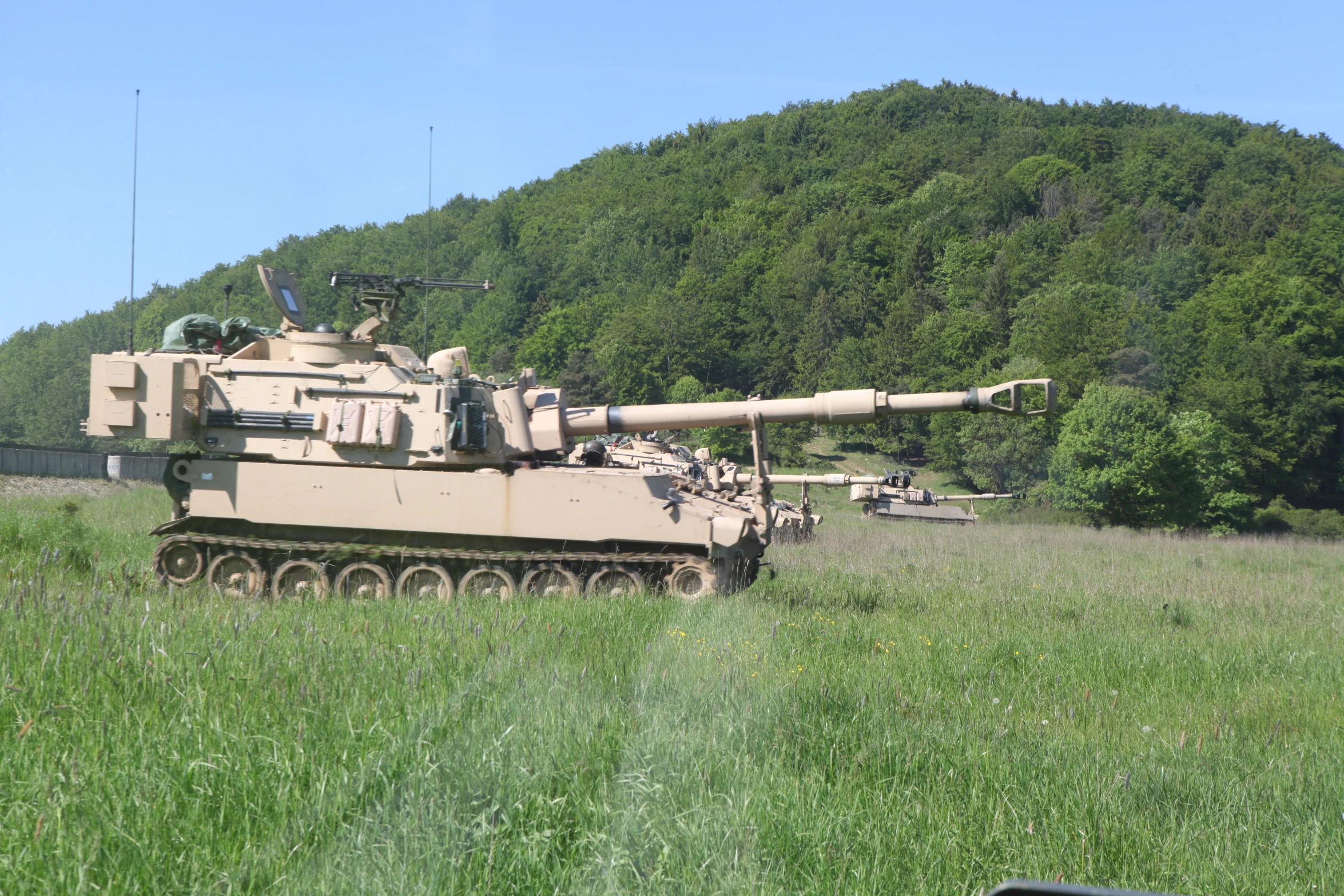 an army tank moving on a track near tall grass