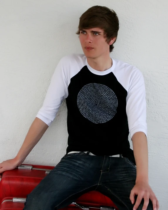 a young man is sitting on luggage in front of a white wall