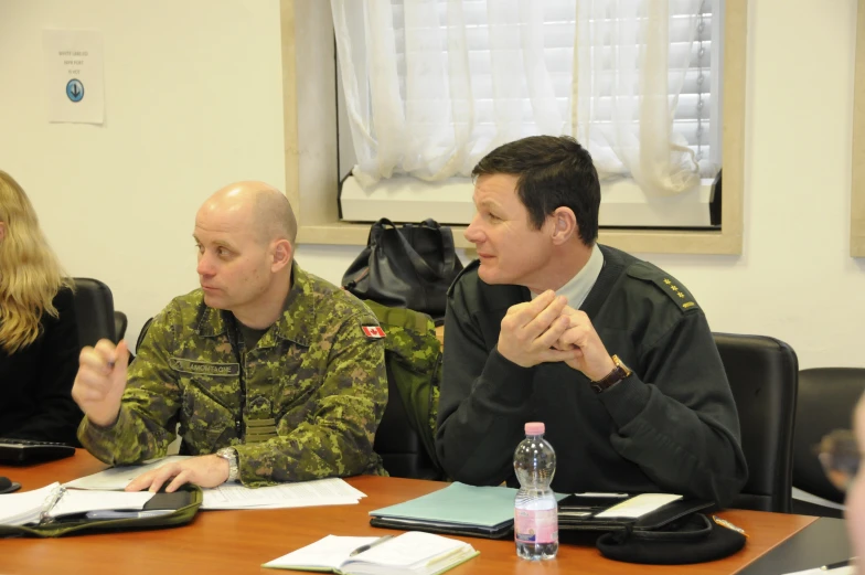 two soldiers sit at a wooden table and look off into the distance