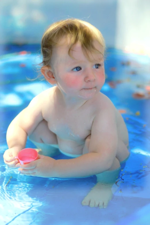 an infant playing in the pool with a pink frisbee