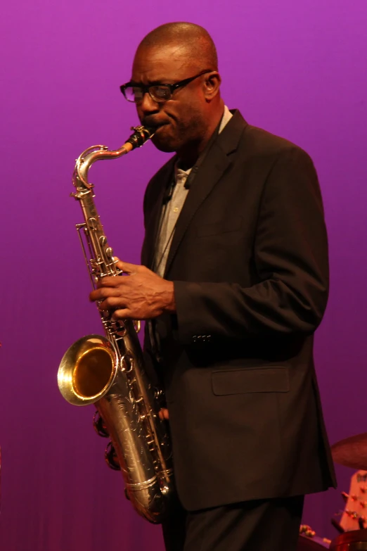 a man with glasses plays a saxophone on a stage