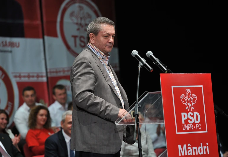 a man stands in front of microphones as others look on