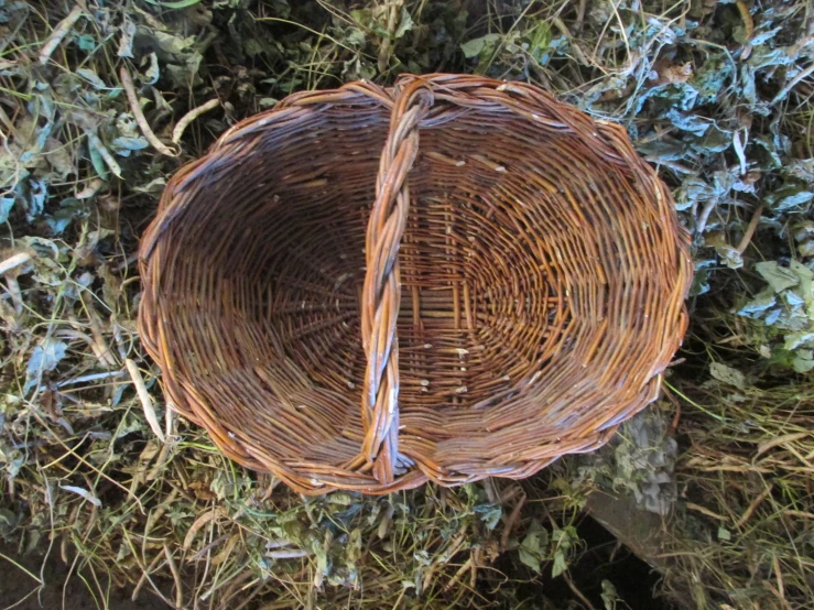 a wicker basket sits on the ground next to twigs