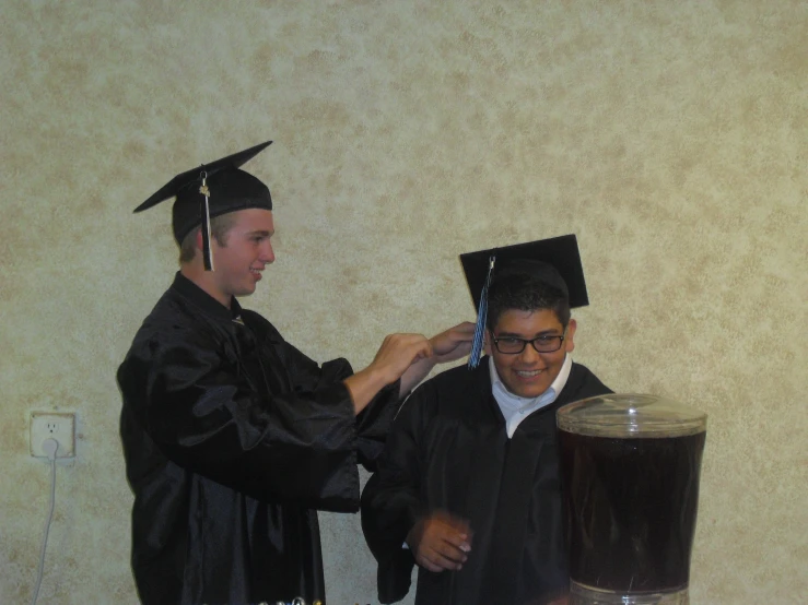 two male graduates standing near a table and one is having his picture taken