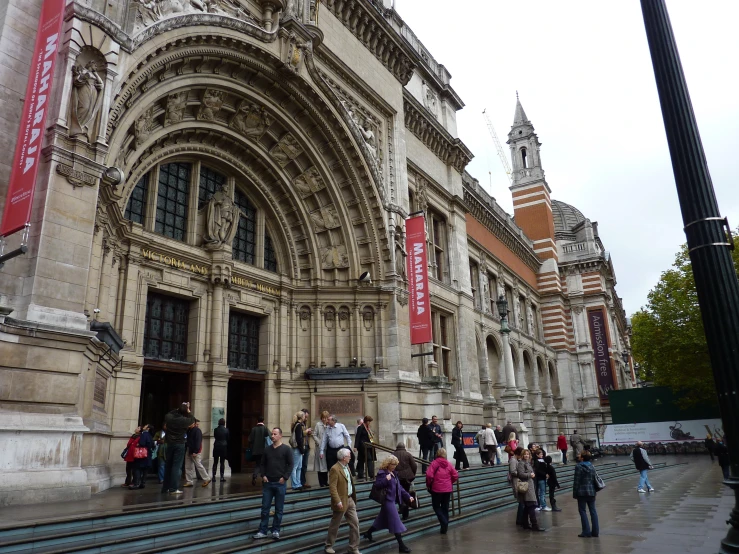 a large group of people walking up a stairway near a stone building