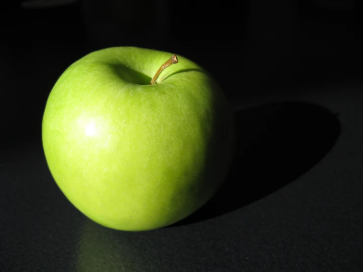 the small green apple is sitting on a black table