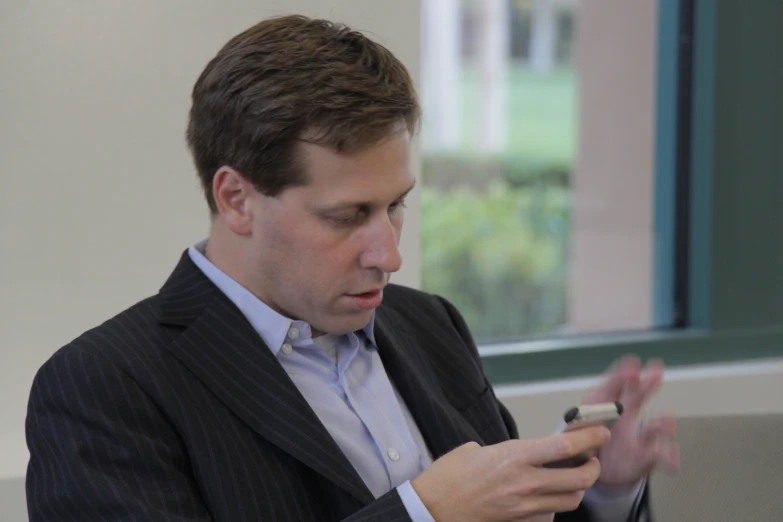 a man with a white shirt and a jacket in front of a window, holding a cellphone