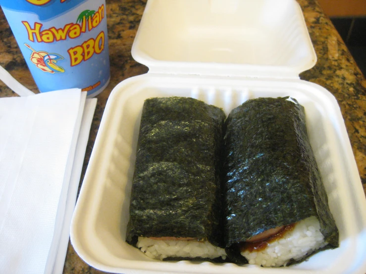 two pieces of sushi sit in a small styrofoam container with a drink