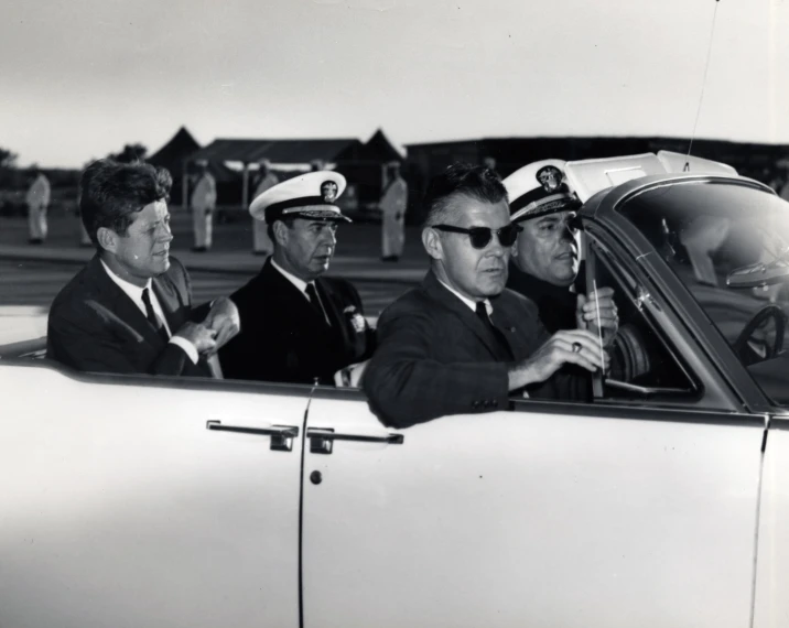 a vintage po shows a man holding soing in his hand while a group of pilots sit next to him in a car