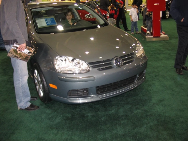 a gray car is parked in front of people on green carpet