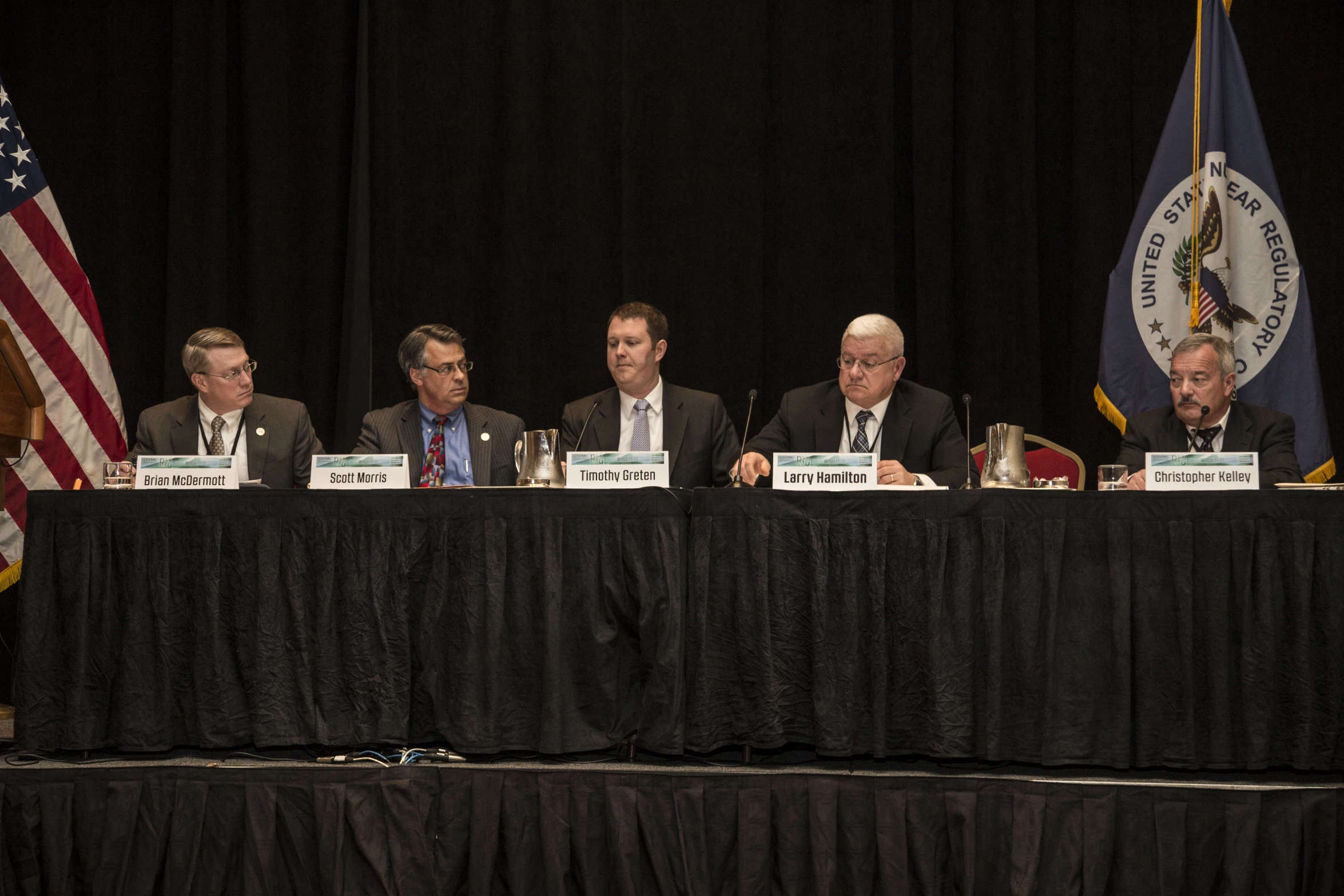 four people sit at a panel with flags in the background