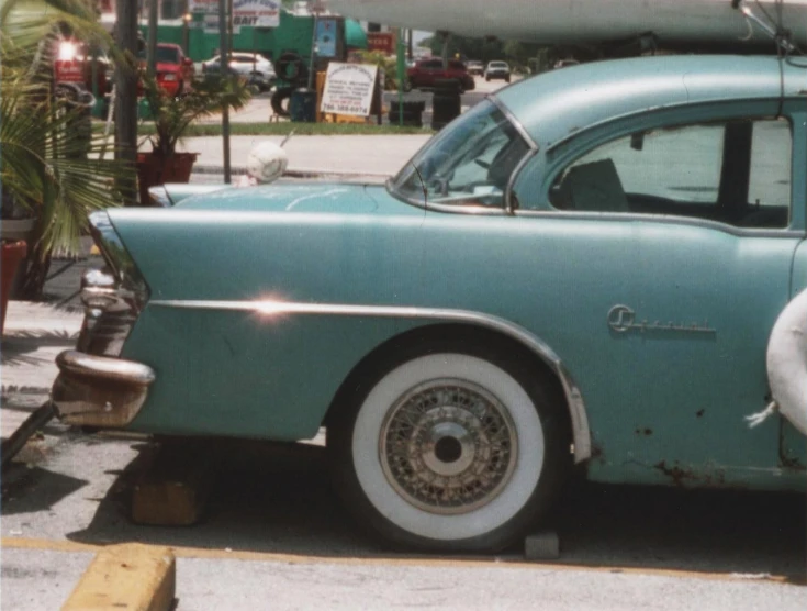 a green old car parked on the street with a surfboard mounted to the side