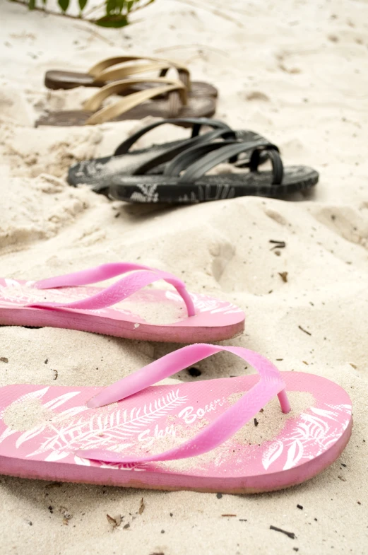 three pairs of flip flops are laid out in the sand