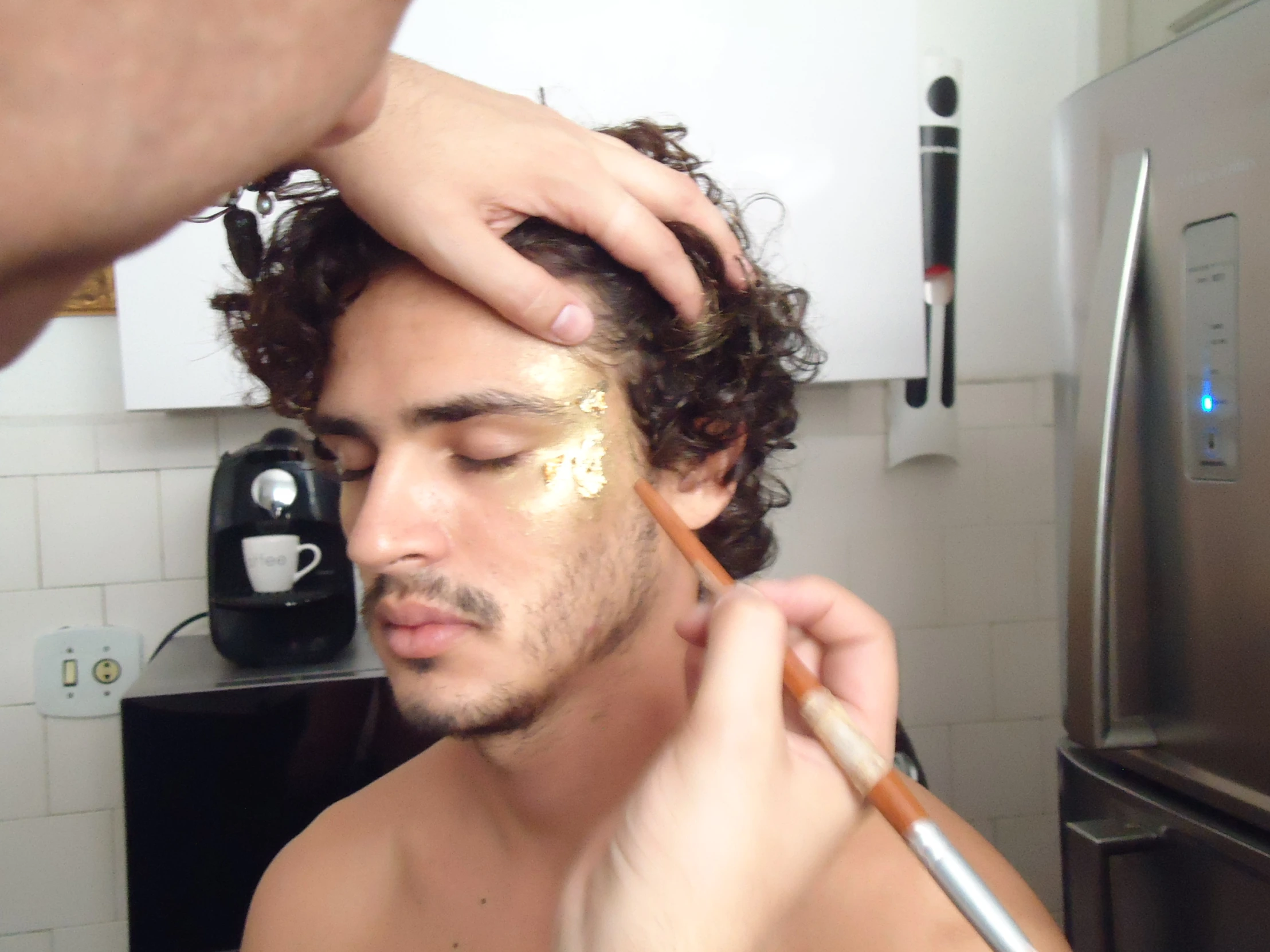 a man is getting his makeup done in the kitchen