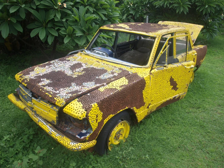 an old yellow car with floral paint is parked in the grass