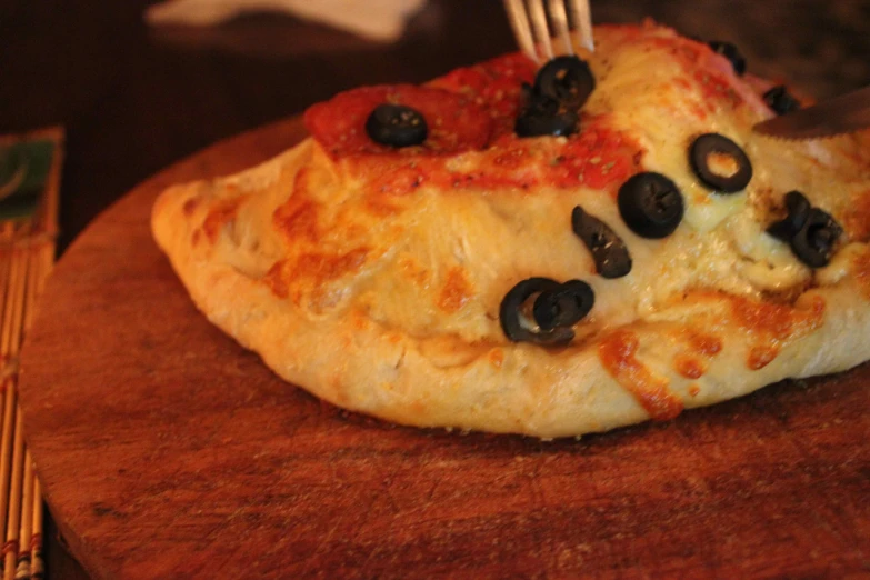 a pizza with olives on it is sitting on a board