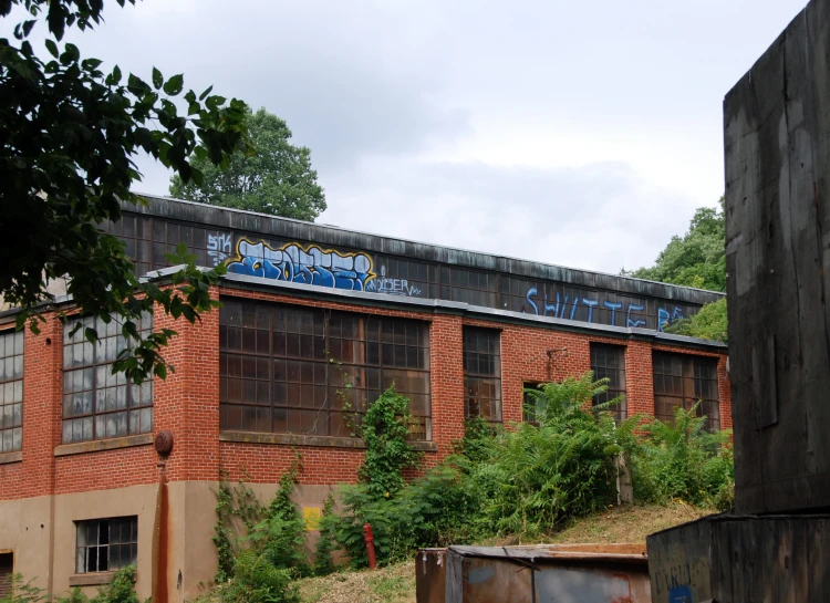 an abandoned building with graffiti on the side and green bushes around