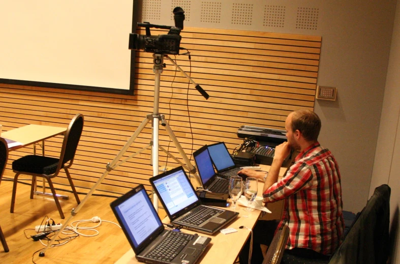 a man on his cell phone in front of a screen with laptops