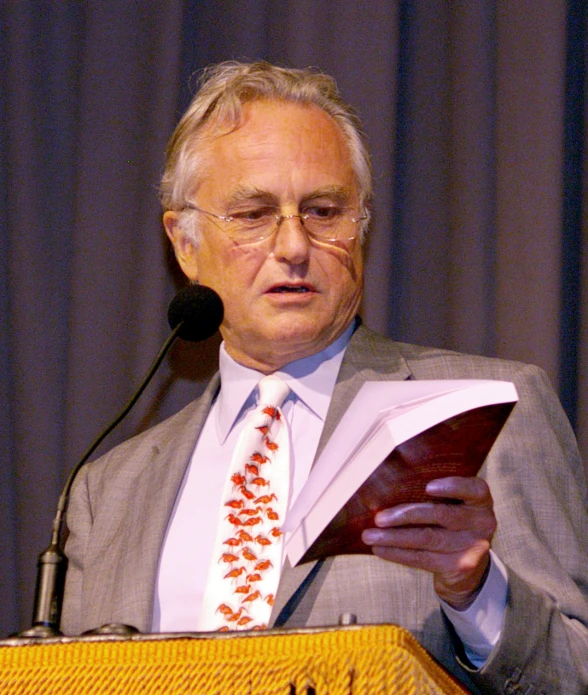 a man wearing glasses and a tie holds a piece of paper at a podium