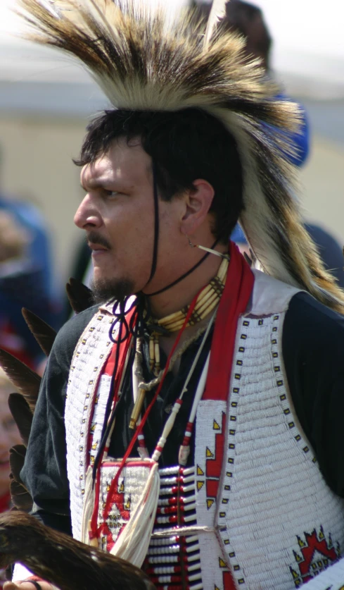 man in native costume with long hair standing at a fair