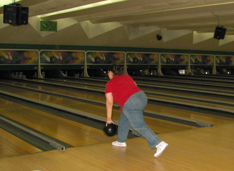 woman bending over holding bowling ball while standing near bowling alley