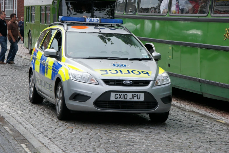 a police car parked next to a street with people walking around