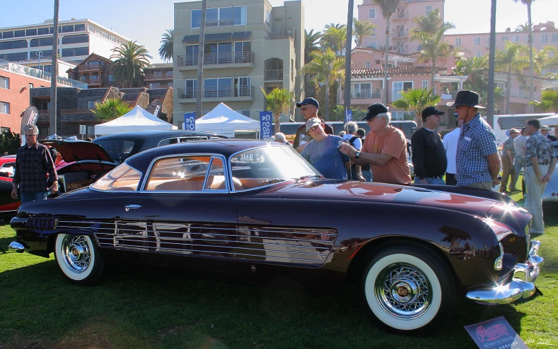 people look at an antique car on display in a city park