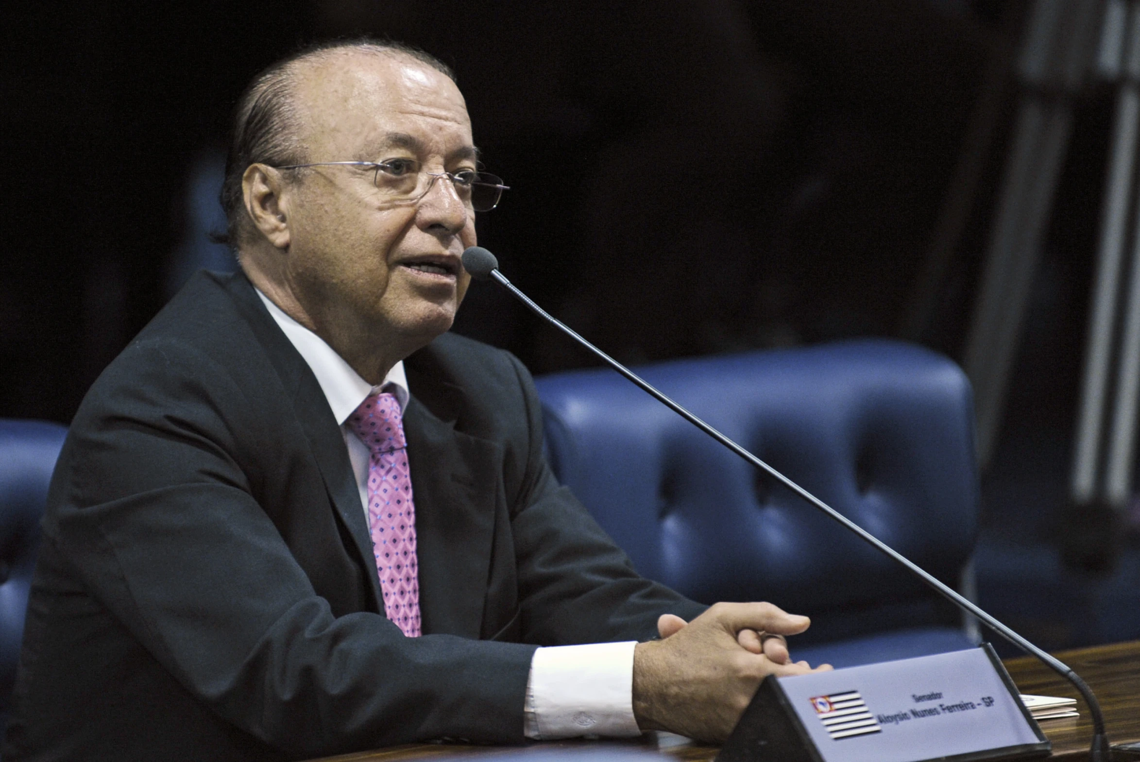 the speaker speaks into his microphone in front of the blue chairs