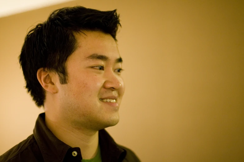 a man smiling in a room with a dark green shirt