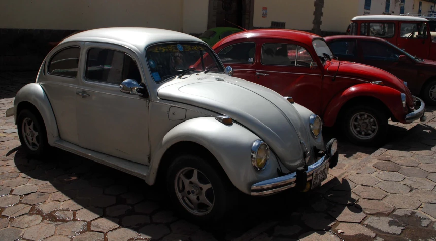 two small vintage vw bug's sit parked on a stone street