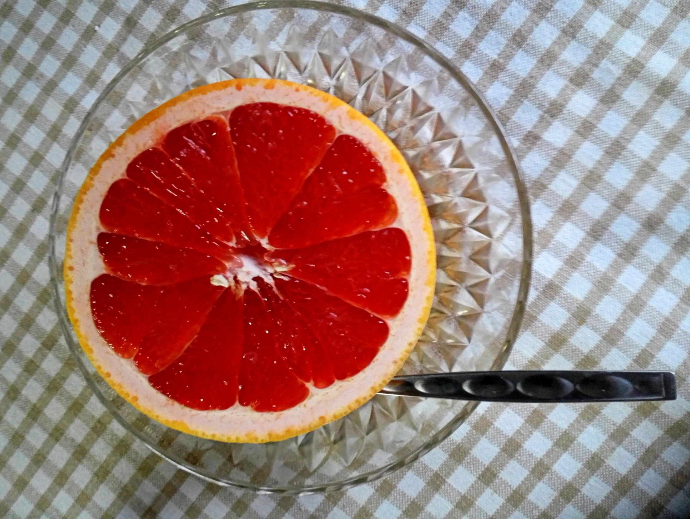 half of gfruit sitting in a glass bowl next to a utensil