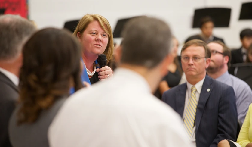 there is a woman standing in front of some people talking