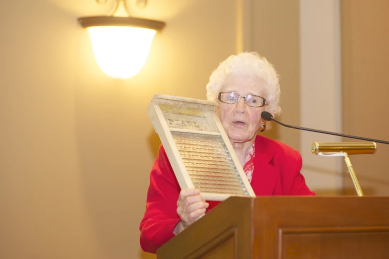 the older woman is at a podium while reading her book