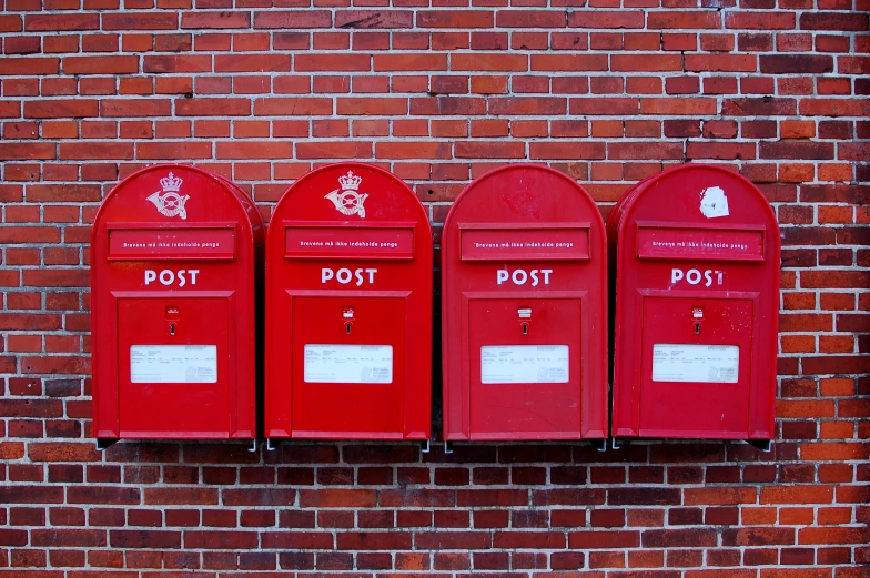 three red post office mail boxes on a brick wall