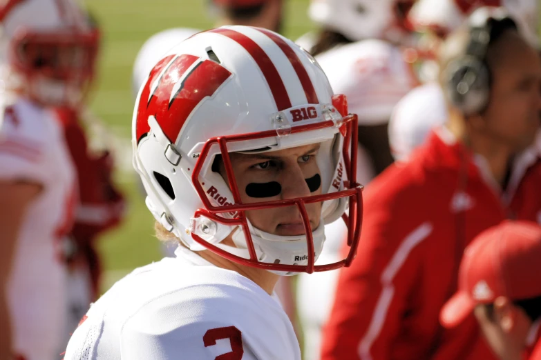 a young man wearing a football helmet with other people standing behind him