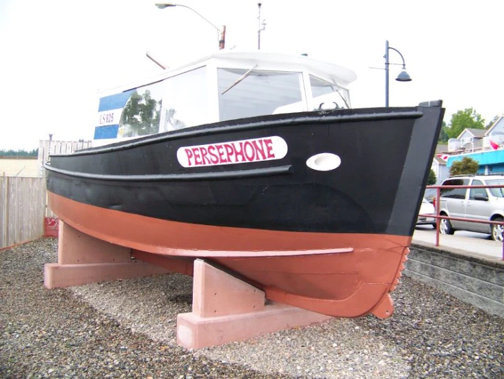 a black and brown boat sitting on gravel next to a fence
