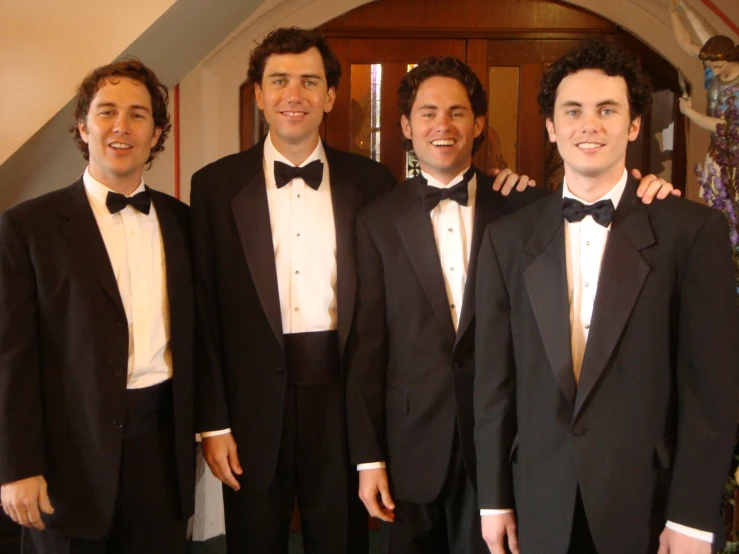 four men posing together for a picture together in black suits