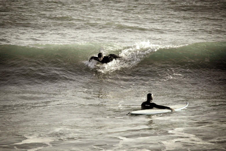 two people in the ocean one on surfboard one surfing