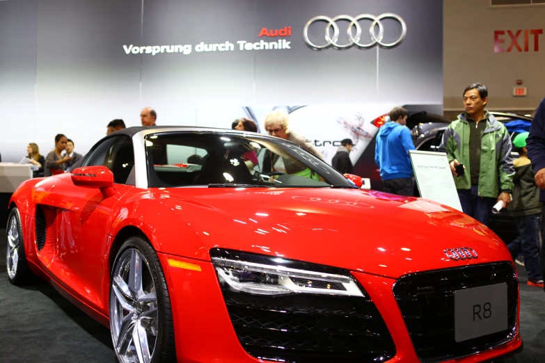 people walk near a red car at an auto show