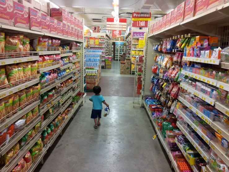 a boy is hing a cart through the aisles of a store