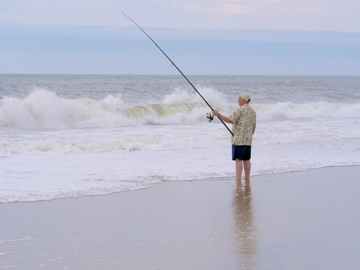a man standing in the sand fishing while holding a fishing pole