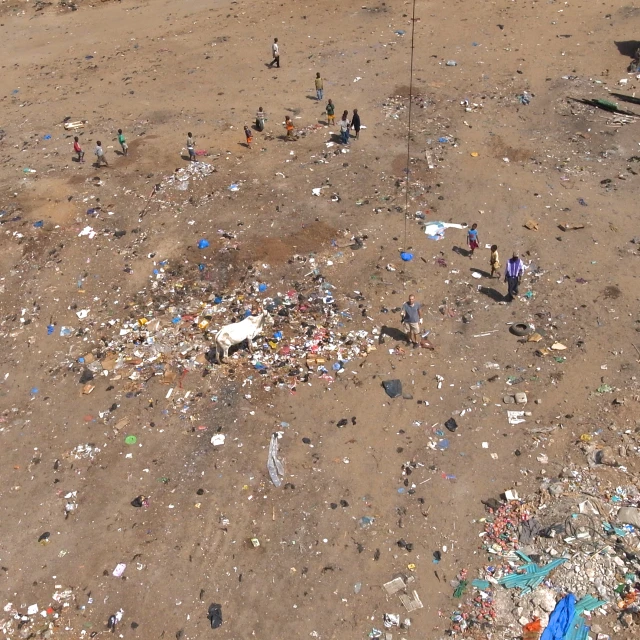 people gather around a small mound of trash in the middle of a dirt area