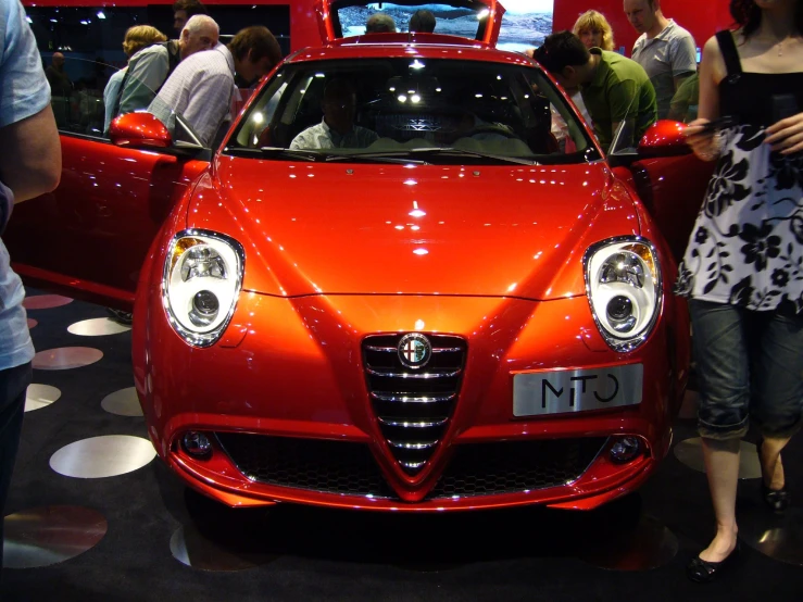 people looking at a red car on display