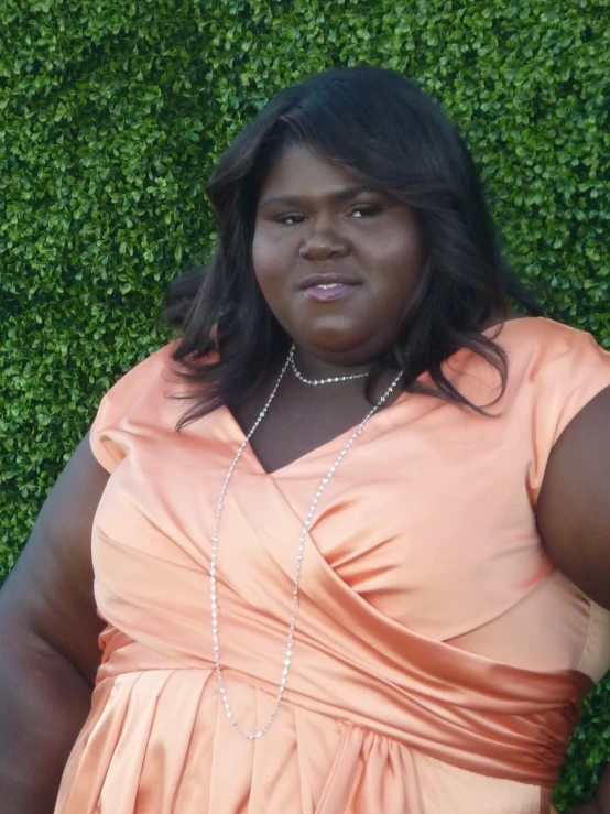 a woman wearing an orange dress is standing in front of a hedge