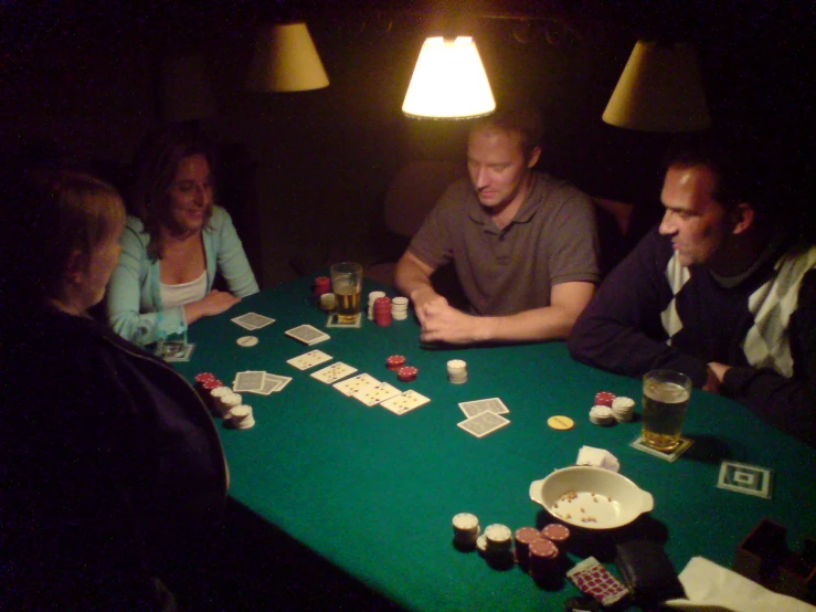 five people sit at a table with playing cards in front of them