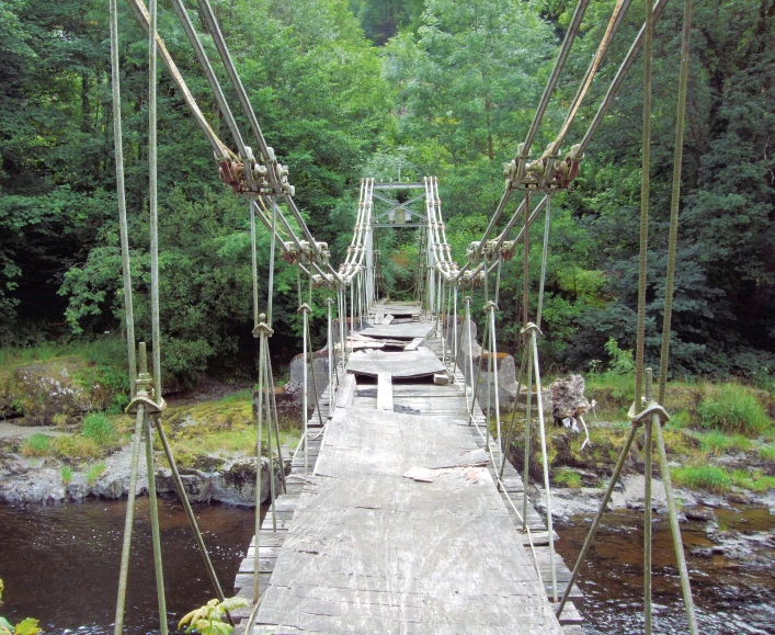a wooden suspension bridge crossing water in the forest