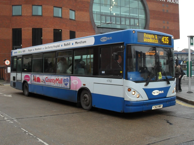 a large blue and white bus driving next to a brick building